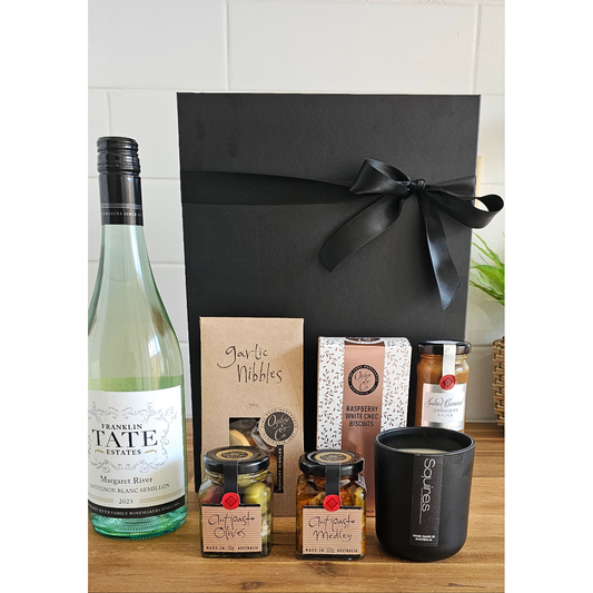 A gift hamper containing a bottle of wine, a soy wax candle, and various gourmet treats